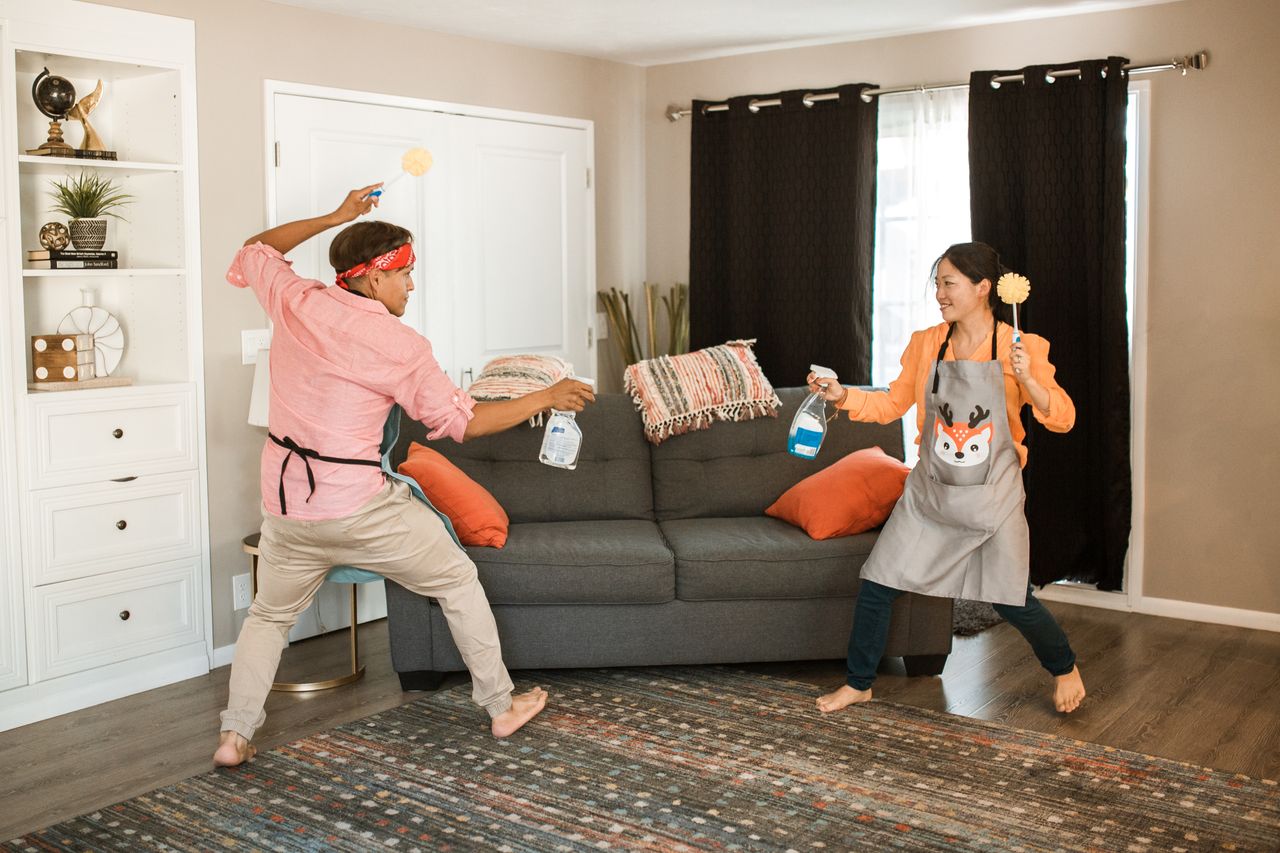 team-03 A joyful couple engages in a playful cleaning fight in their living room, showcasing light-hearted domestic life.