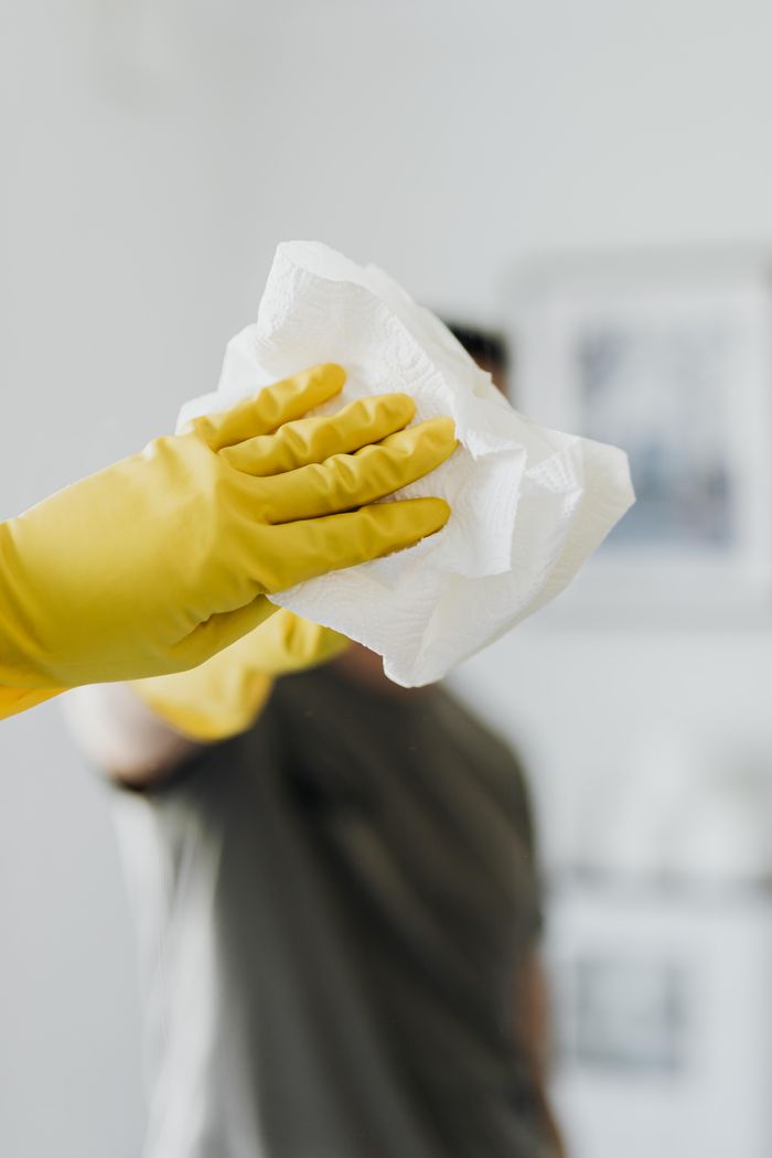 who-we-are Anonymous male wearing yellow latex gloves and dark t shirt wiping mirror in bathroom with paper napkin
